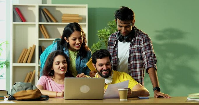 Using laptop for group assignment, Indian college students studying with books and notes in library, learning together in teamwork, sharing knowledge in educational atmosphere indoors