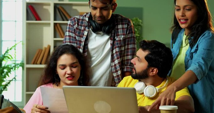 Using laptop for group assignment, Indian college students studying with books and notes in library, learning together in teamwork, sharing knowledge in educational atmosphere indoors