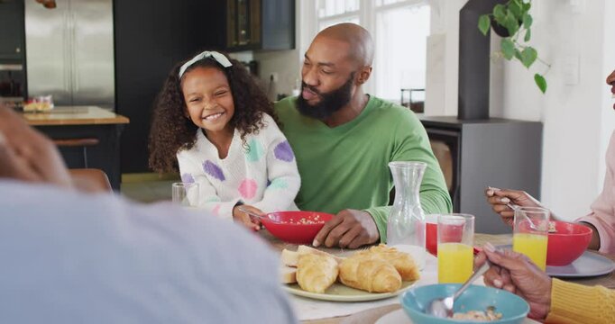 Video of happy african american daughter laughing and feeding father at family breakfast table