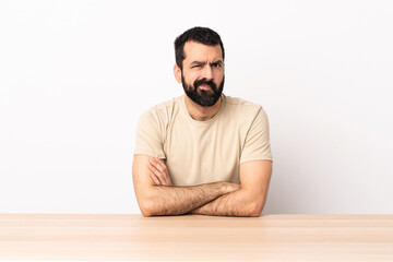 Caucasian man with beard in a table with unhappy expression.