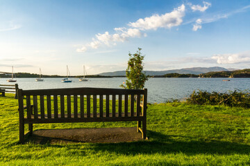 Obraz premium Empty bench overlooking scenic bay with sailboats in Isle of Skye, Scottish Highlands, Scotland.