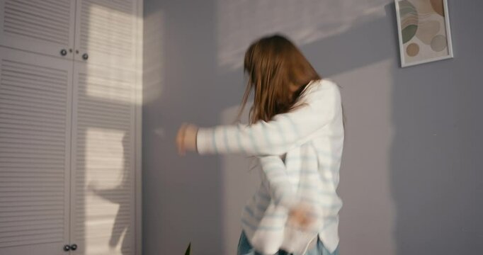 Cheerful girl in casual clothes dancing and moving energetically while listening to cheerful and upbeat rock music at home