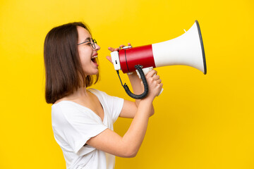 Young Ukrainian woman isolated on yellow background shouting through a megaphone to announce...