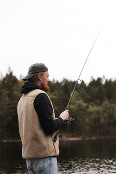 Man fishing at forest lake on calm overcast day