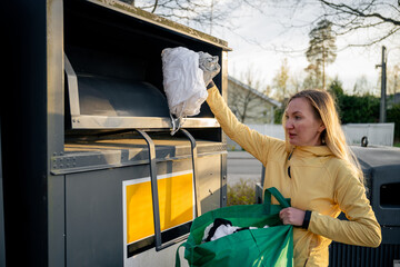 Woman placing old used clothes at recycling bins