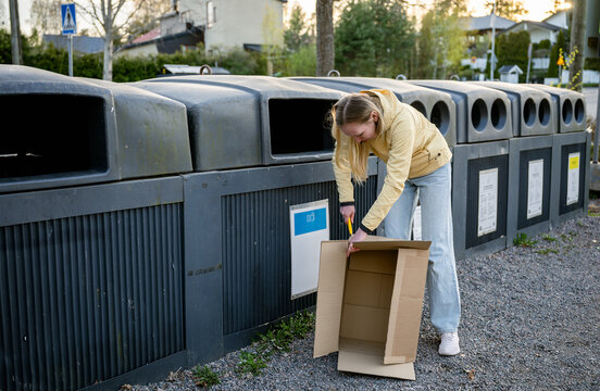 woman puts cardboard trash in outdoor recycling bins