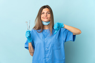 Slovak dentist holding tools isolated on blue background showing thumb down with negative expression