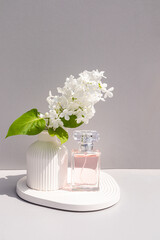 Beautiful spring still image with women's perfume in a bottle on a tray with a vase with a branch of white lilac. A blank bottle mockup. Front view.