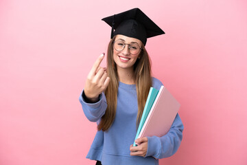 Young student woman wearing a graduate hat isolated on pink background doing coming gesture
