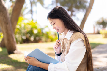 Obraz premium Pretty Chinese woman at outdoors holding a notebook