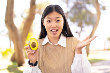 Pretty Chinese woman holding an avocado at outdoors with shocked facial expression