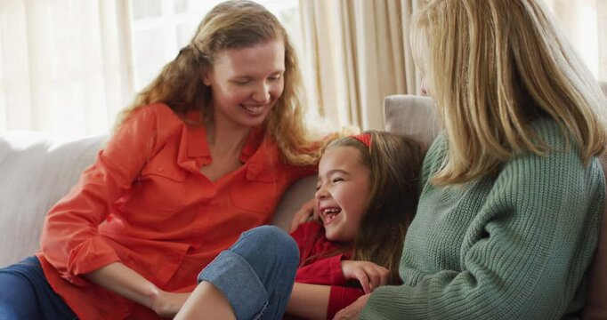 Video of happy caucasian daughter tickled by mother and grandmother sitting on couch