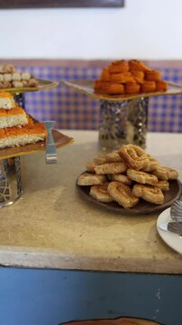 Vertical screen layers of basbousa topped with crisp orange kataifi stacked neatly on a golden tray create a striking contrast of textures in a bright Middle Eastern dessert display