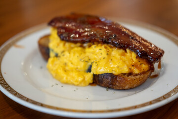 Toast topped with scrambled eggs and thick cut bacon, served on a plate 
