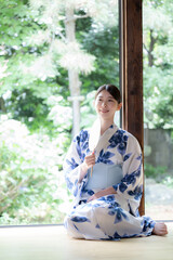 縁側に座る団扇を持った浴衣の女性の全身
