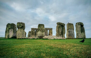 Naklejka premium Stonehenge under a cloudy sky with green grass and a crow.
