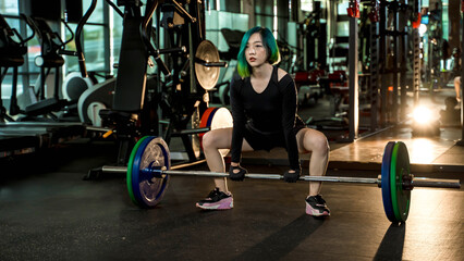 Strong young woman preparing for sumo deadlift with heavy barbell in gym, wearing black athletic outfit, focus and power in strength training