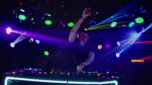 A DJ in a club setting, captured from a low-angle shot, mixes tracks with colorful lights and fog, creating a dynamic video atmosphere.