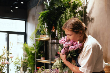 Middle-aged female florist in apron arranging fresh flowers for bouquet in the flower shop. Small...
