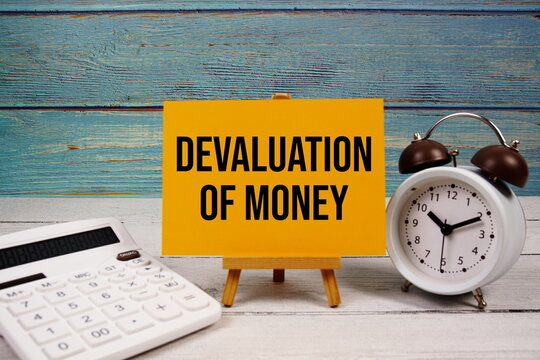 Devaluation Of Money text written on paper card with calculator and alarm clock on wooden background