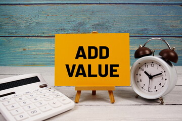 Add Value text written on paper card with calculator and alarm clock on wooden background