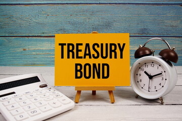 Treasury Bond text written on paper card with calculator and alarm clock on wooden background