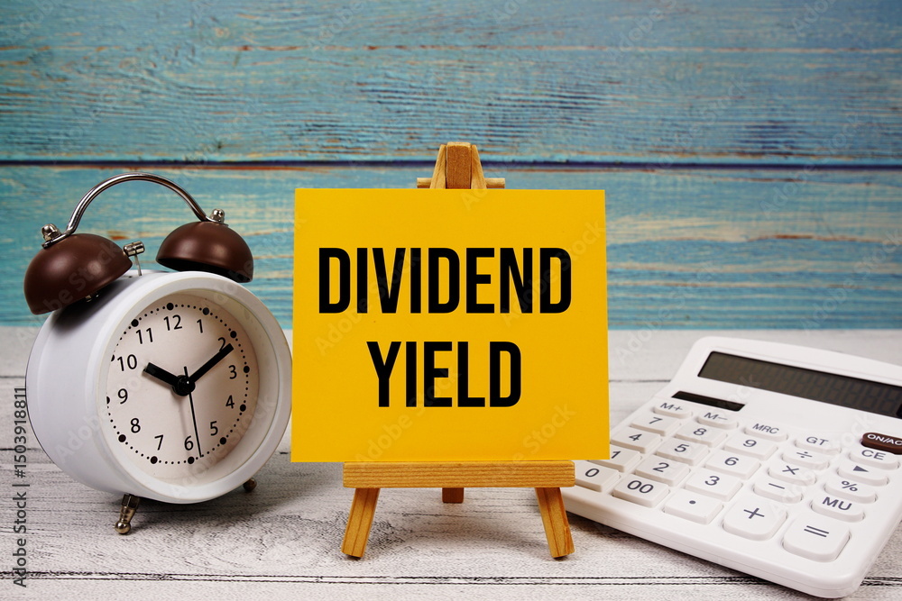 Poster dividend yield text written on paper card with calculator and alarm clock on wooden background
