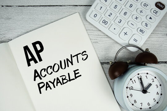 AP Accounts Payable text on paper notebook page with alarm clock and calculator on wooden background