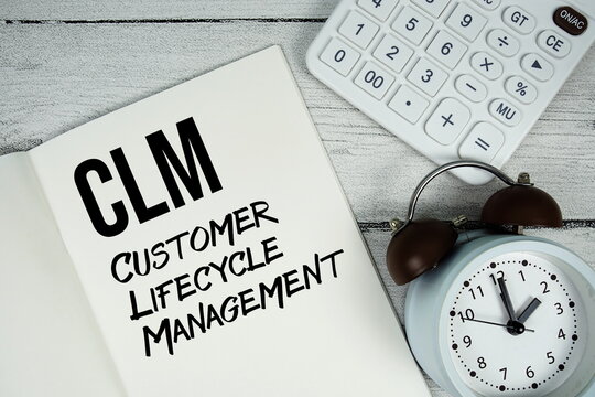 CLM Customer Lifecycle Management text on paper notebook page with alarm clock and calculator on wooden background