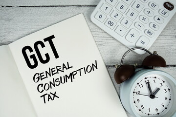 GCT General Consumption Tax text on paper notebook page with alarm clock and calculator on wooden...