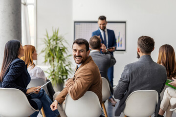 Portrait of smiling manager sitting at boardroom during presentation and looking over shoulder at...