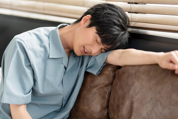 体調不良の若い日本人男性。彼はソファーに寄りかかっている。