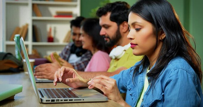 Indian college students using laptop to complete assignment with books, notes, preparing for exams studying in a focused, collaborative environment inside a university campus library in exam season