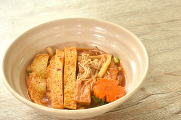 udon noodles topping slice fish tofu and needle mushroom with carot in kimchi soup on bowl