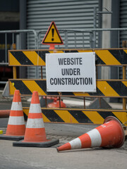 Construction barrier with a website under construction sign and traffic cones on the street.