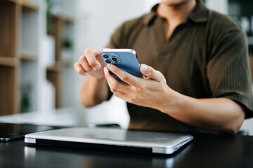 Closeup of a man using a smartphone at a desk with a laptop. Modern digital lifestyle, perfect for business, and mobile app