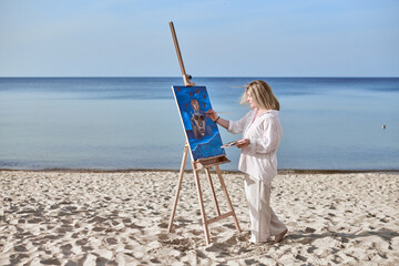 Young woman artist stands near ocean, painting on easel. Serene beach environment complements her...