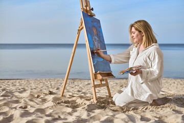 Young woman paints on beach, blending tranquility of ocean with artistic expression. Vibrant scene...