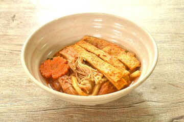 udon noodles topping slice fish tofu and needle mushroom with carot in kimchi soup on bowl