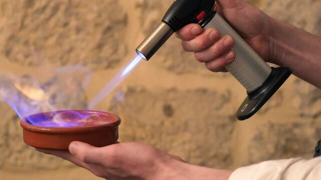 Close-up of hand torching sugar on cr&egrave;me br&ucirc;l&eacute;e to create a golden caramelized crust