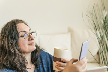 woman looking at smartphone while drinking coffee