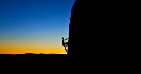 A silhouette of a person rock climbing on a large rock formation during a beautiful sunset. The...