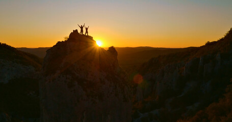 A breathtaking aerial view showcases two climbers reaching the summit of a towering rock formation...