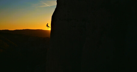 A daring rock climber defies gravity as they scale a steep cliff at sunset. The breathtaking aerial...