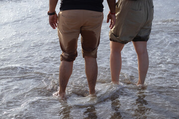 Beautiful young couple enjoying the weekend with barefoot in the beach with the water being filled their legs during morning golden hours