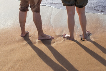 Young couples standing on the beach sand which is covered with water and wet, and couples shadow beautifully reflected on the sand during golden hours in the morning