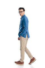 Naklejka premium side view of smart casual man with glasses walking with hand in pocket