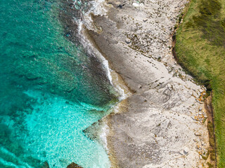 Aesthetic summer background. A top-down aerial photo capturing the transition from grassy terrain to bright limestone and shallow, crystal-clear water