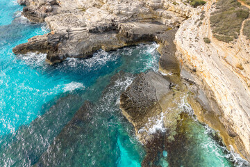 drone view of steep cliffs and rocky outcrops dipping into the Adriatic Sea. The dramatic contrast between rough stone and vivid water highlights the raw power of nature