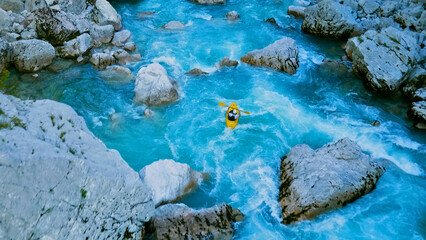 A person navigates a yellow kayak through a narrow, rocky river, surrounded by large boulders and strong currents. This aerial view highlights the thrill and challenge of extreme kayaking in a.